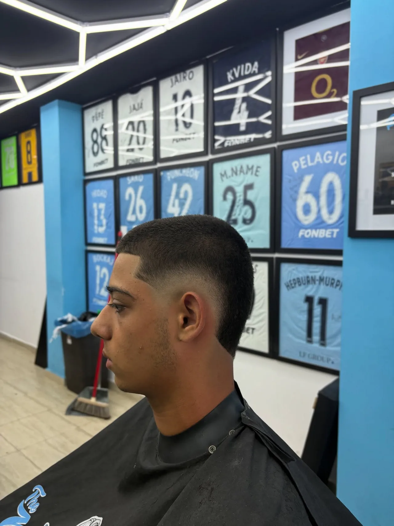 Client with a fresh fade in front of the wall of framed football shirts